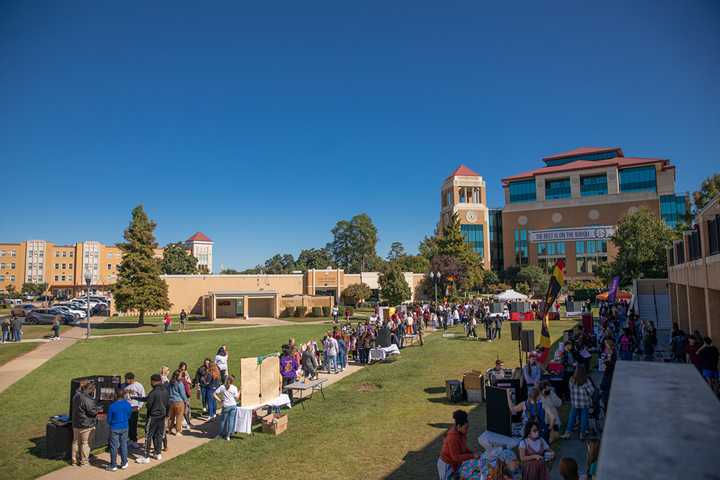 People mingle at booths and tables in the quad on Ƶ's campus. A banner hanging from the library in the background reads "The Best is on the Bayou."